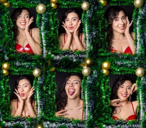 Cheerful woman in a red satin dress posing playfully amidst festive green tinsel decorations.