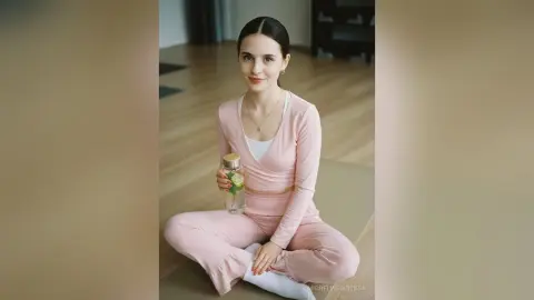 Young woman in pink loungewear sitting on a yoga mat in a bright, minimalist room with a calm mood.