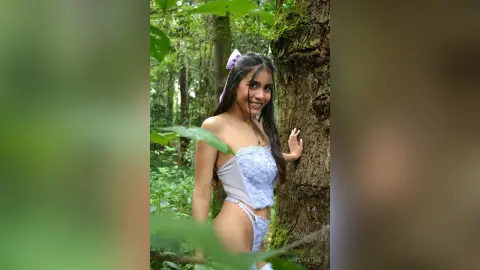 AmeliaStell smiles while leaning against a large tree trunk in a forest, wearing a light blue lace lingerie set.