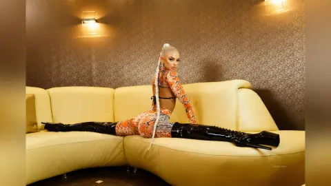 Anastasia spreads her legs in a split while wearing an orange patterned bra and matching bottoms with long black thigh-high boots.