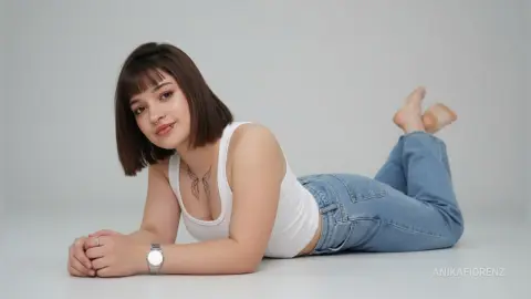 Young woman with short brown hair in a white tank top and blue jeans lying on a white floor with a relaxed mood.
