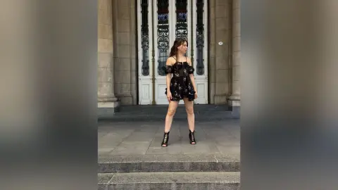 Elegant woman in a black sequin cocktail dress standing before ornate classical doors in a moody urban setting.