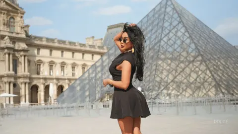 Dolce poses in a short black dress and sunglasses in front of the glass pyramid in Paris.