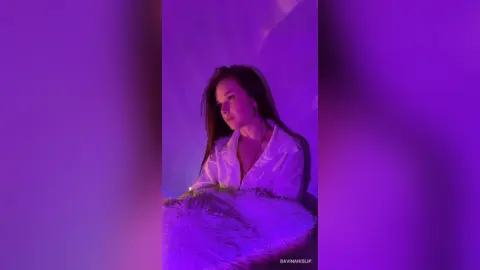 Young woman in a white shirt sitting in moody purple lighting with a soft faux fur texture.