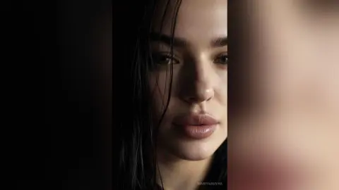 Close-up portrait of a woman with wet hair and natural makeup looking moody in soft, dramatic lighting.