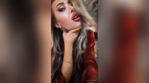 Glamorous woman with blonde hair and red lipstick wearing a red outfit in a moody, close-up portrait.