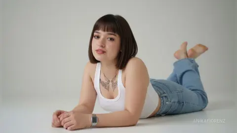 Young woman with short brown hair in a white tank top and blue jeans lying on a white floor.
