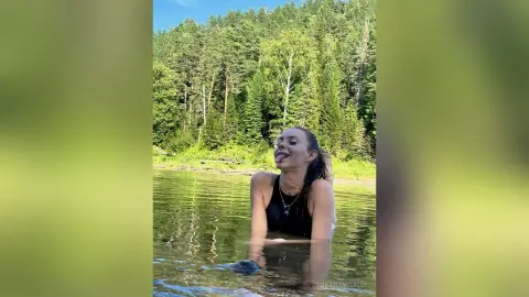 Playful young woman in a black tank top relaxing in a calm forest lake during a sunny summer day.