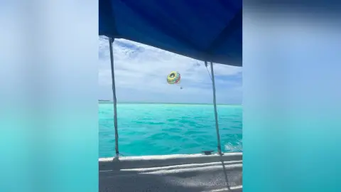 Colorful hot air balloon floating over turquoise tropical ocean waters under a bright blue sky.