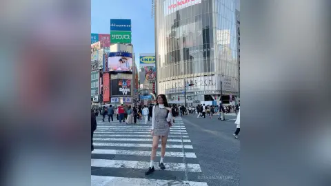 Stylish woman in a white blouse and plaid skirt walking through a busy Tokyo street near Shibuya crossing.