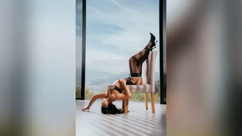 Glamorous woman in black lingerie and stockings reclining on a chair in a bright, modern minimalist room.