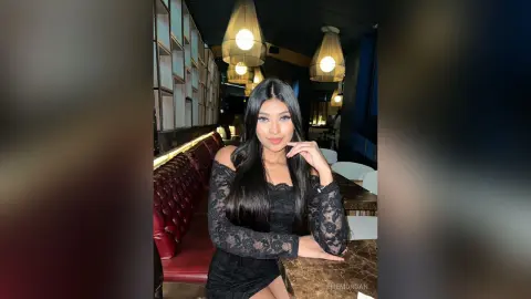 Beautiful woman in a black lace dress sitting at a restaurant bar under warm ambient lighting.