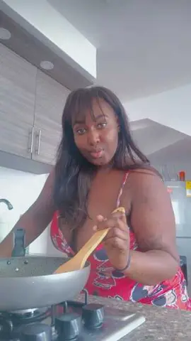 Smiling woman in a red floral dress cooking in a bright modern kitchen.