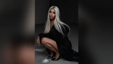 Glamorous blonde woman in a black faux fur coat posing in a moody studio setting.
