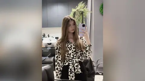 Young woman in a leopard print blouse taking a mirror selfie in a modern salon setting.