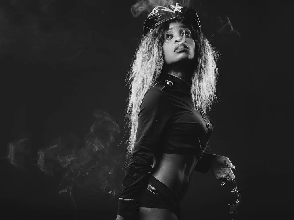 Moody black and white portrait of a glamorous woman in a dark outfit posing amidst swirling smoke.