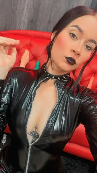 DollDolly wears a black leather top and a studded choker while posing for a close-up shot.