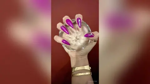 Close-up of long stiletto purple manicured nails held against a crystal glass bowl for a glamorous beauty look.
