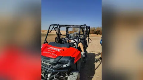 AnnaBanks sits in a red off-road buggy in the desert, wearing a white tank top and a blue headwrap or mask.