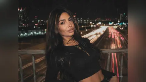 Beautiful woman in a black crop top posing on a city bridge at night with blurred highway lights in the background.
