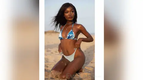 Beautiful Black woman in a blue patterned bikini relaxing on a sunny beach at sunset.