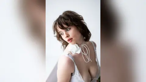 Dreamy portrait of a young woman in a white lace outfit against a bright, minimalist background.