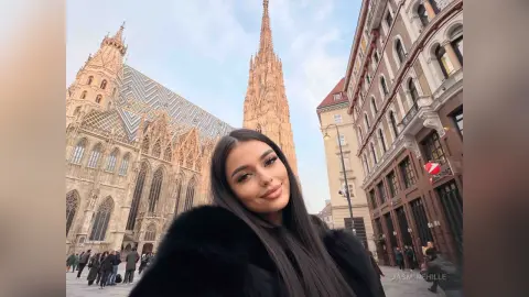 Young woman in a black faux fur coat smiling in front of the historic Gothic architecture of St. Stephen's Cathedral.