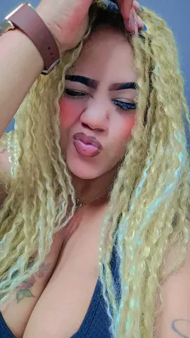 Blonde woman with wavy hair and pink blush wearing a black tank top in a playful mood.