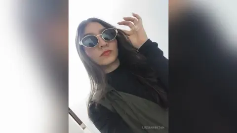 Young woman in black top and round sunglasses posing with a cool, stylish aesthetic against a white background.