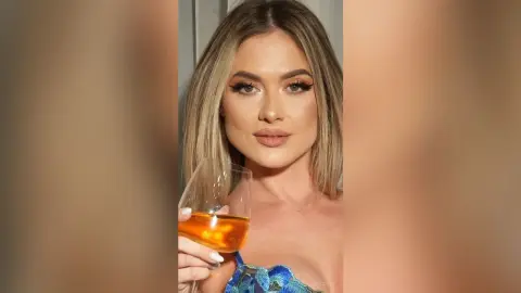 Glamorous woman with winged eyeliner holding a glass of white wine in a sophisticated evening setting.