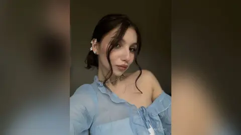 Young woman in a light blue ruffled blouse with silver jewelry posing with a soft, elegant expression.