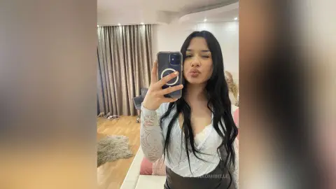 Young woman in a white lace top taking a playful selfie in a modern living room setting.