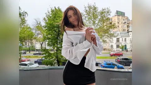 Smiling woman in a white off-the-shoulder blouse and black skirt standing outdoors near city trees.