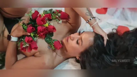 Woman lying on white bedding covered in red roses for a romantic and moody floral aesthetic.