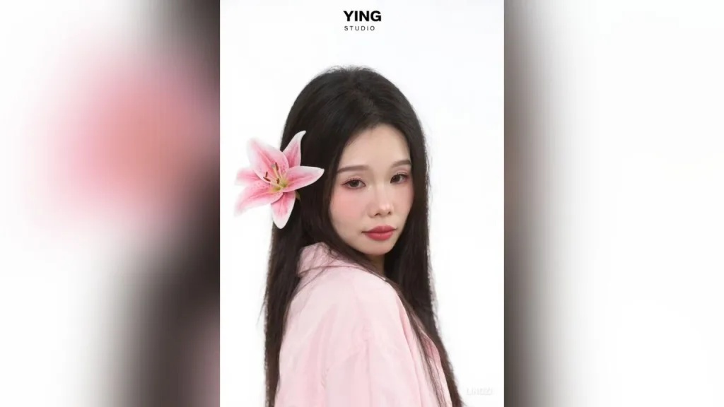 lingzi — lingzi poses with a pink lily flower tucked behind her ear against a white background.