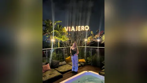 Stylish woman in black top and light blue jeans sitting on a lounge sofa at Viajero outdoor night lounge.