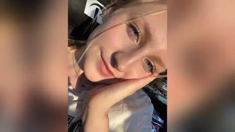 Close-up portrait of a blonde woman with blue eyes smiling warmly in soft natural sunlight.