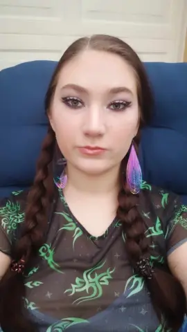 jenellehayesxoxo looks at the camera with long dark hair in braids and wearing a black and green patterned mesh top.