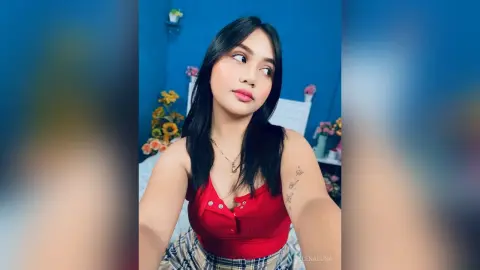 Young woman in a red tank top and plaid skirt posing in a blue bedroom setting with a soft, dreamy mood.