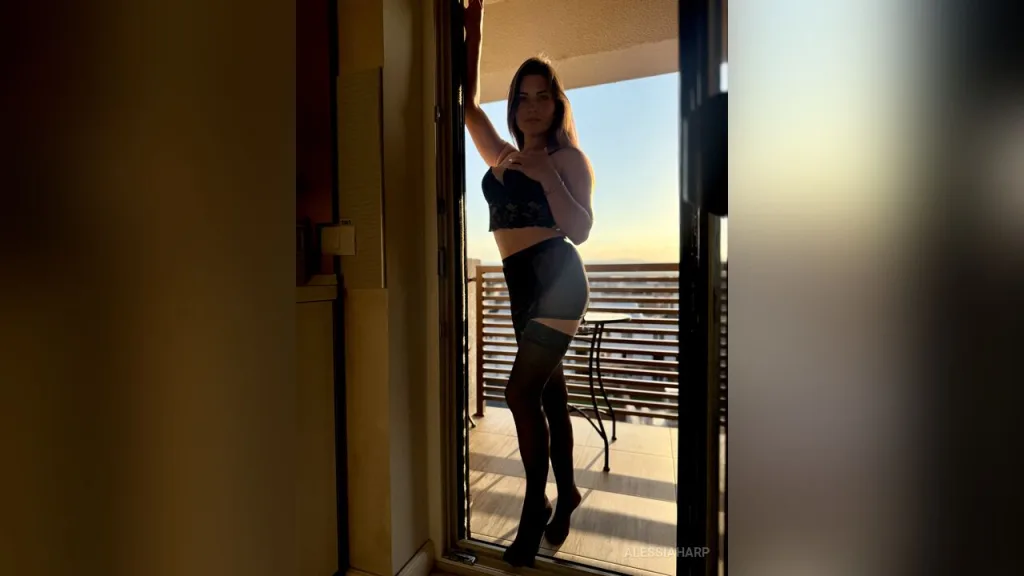 AlessiaHarp — AlessiaHarp stands in a doorway wearing a black lace bra, a grey skirt, and black stockings.