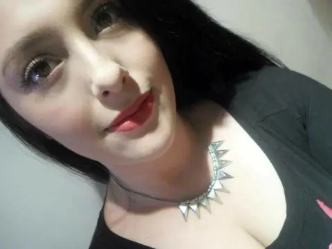Young woman with long dark hair wearing a black t-shirt and silver spiked choker necklace in a soft indoor light.