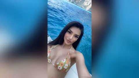 Smiling woman in a floral print bikini relaxing on a boat in the bright blue ocean water.