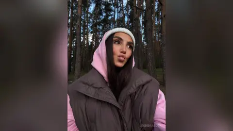 LeonidaAbdon wearing a pink hoodie and white beanie, posing in a forest setting.
