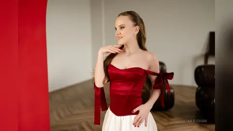 Elegant woman in a red satin corset and white skirt posing in a modern minimalist room.