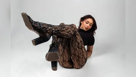 MadisonJane poses in black lace leggings and a black top, sitting on a white floor with her legs raised and wearing black strappy high-heeled sandals.