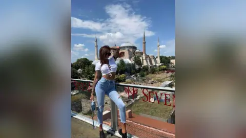 Stylish woman in white crop top and jeans posing on a rooftop overlooking the Hagia Sophia in Istanbul.