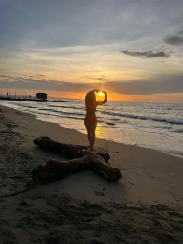 Silhouette of a woman in an orange bikini making a heart shape at the beach during a golden sunset.