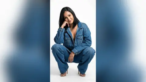 Smiling woman in a denim jacket and jeans posing against a white background for a casual fashion portrait.