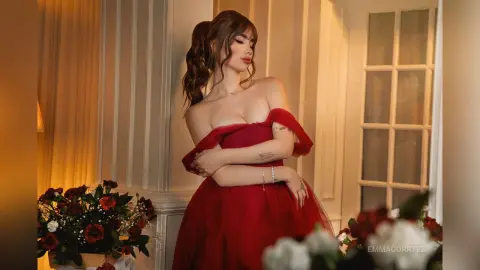 Elegant woman in a red off-the-shoulder gown posing gracefully in a warm, romantic indoor setting.