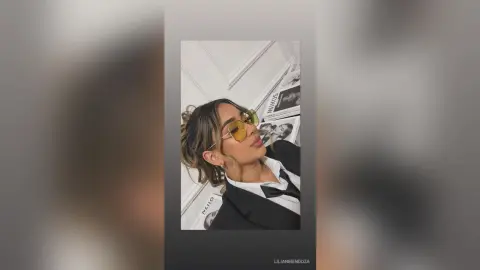 Stylish woman in a black blazer and yellow sunglasses posing indoors with a chic, confident mood.